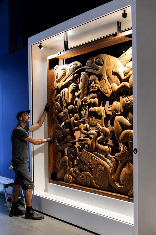 Trent Rucker installing a large carved wooden panel in a museum case